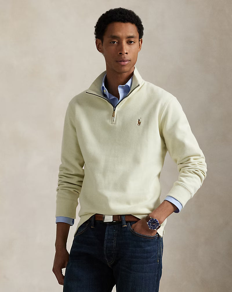 Man wearing a light-colored sweater with a brand logo on a beige background